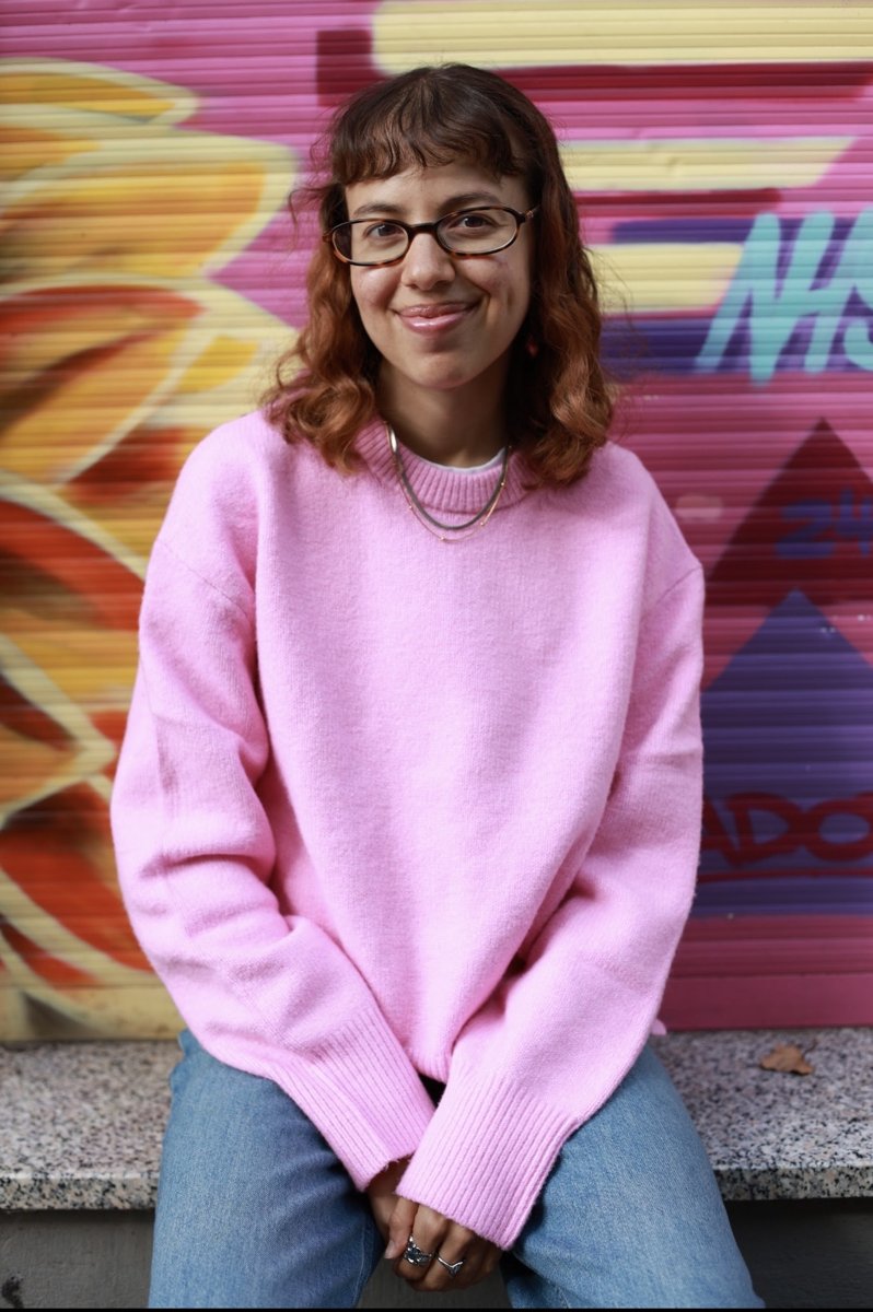 Mica Welpmann con un suéter rosa frente a un mural de colores